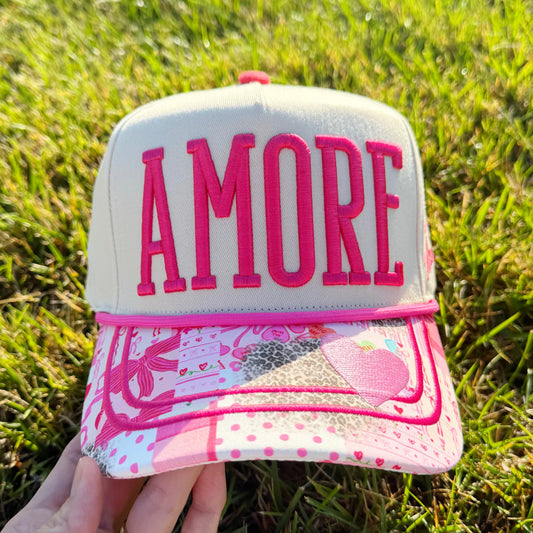 Pink and white cap with 'AMORE' text held in grass