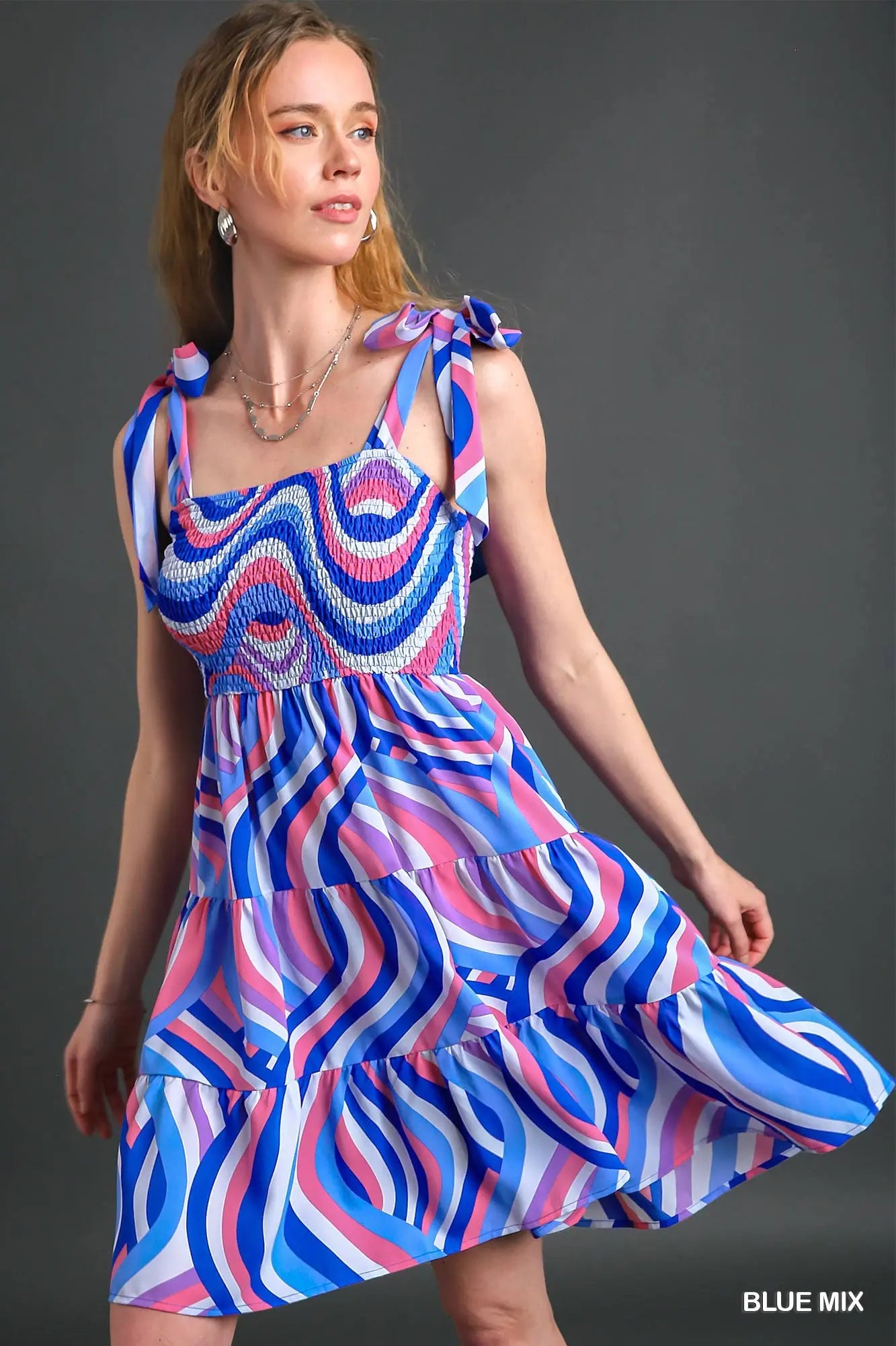 Woman wearing a colorful dress with a blue, pink, and red pattern on a gray background