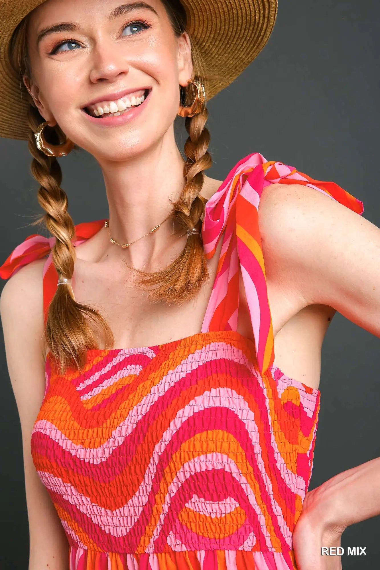 Woman wearing a colorful dress with a straw hat against a gray background