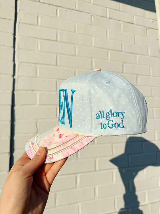 Cap with 'EN' and 'all glory to God' text held against a light brick wall.