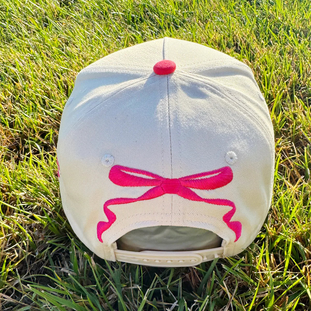 Baseball cap with pink bow design on grass