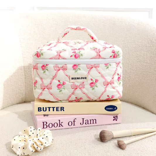 Floral-patterned cosmetic bag on books with makeup tools on a beige surface