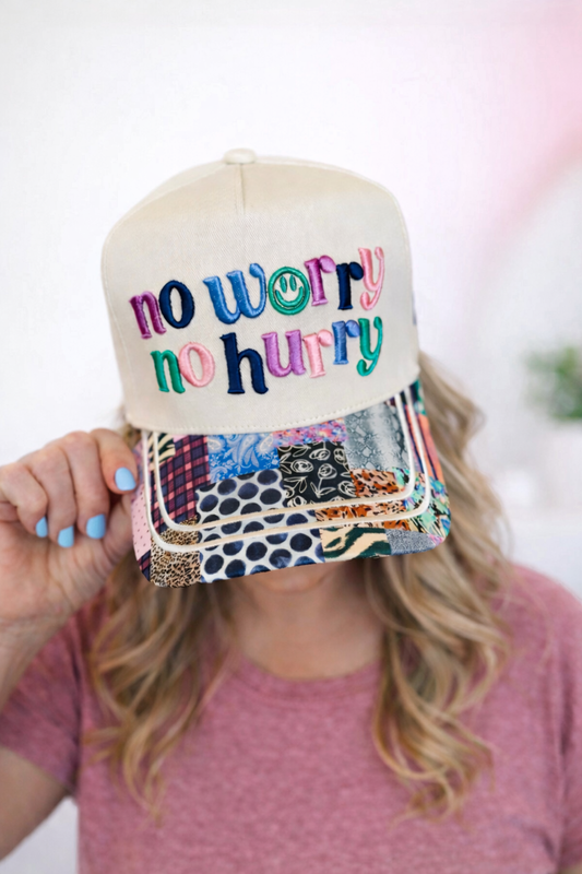Cap with 'no worry no hurry' text held by a person with a blurred background