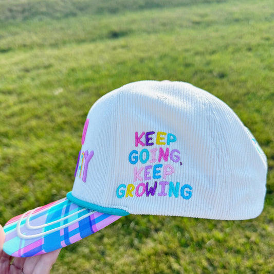 Cap with 'Keep Going, Keep Growing' text held against a grassy background