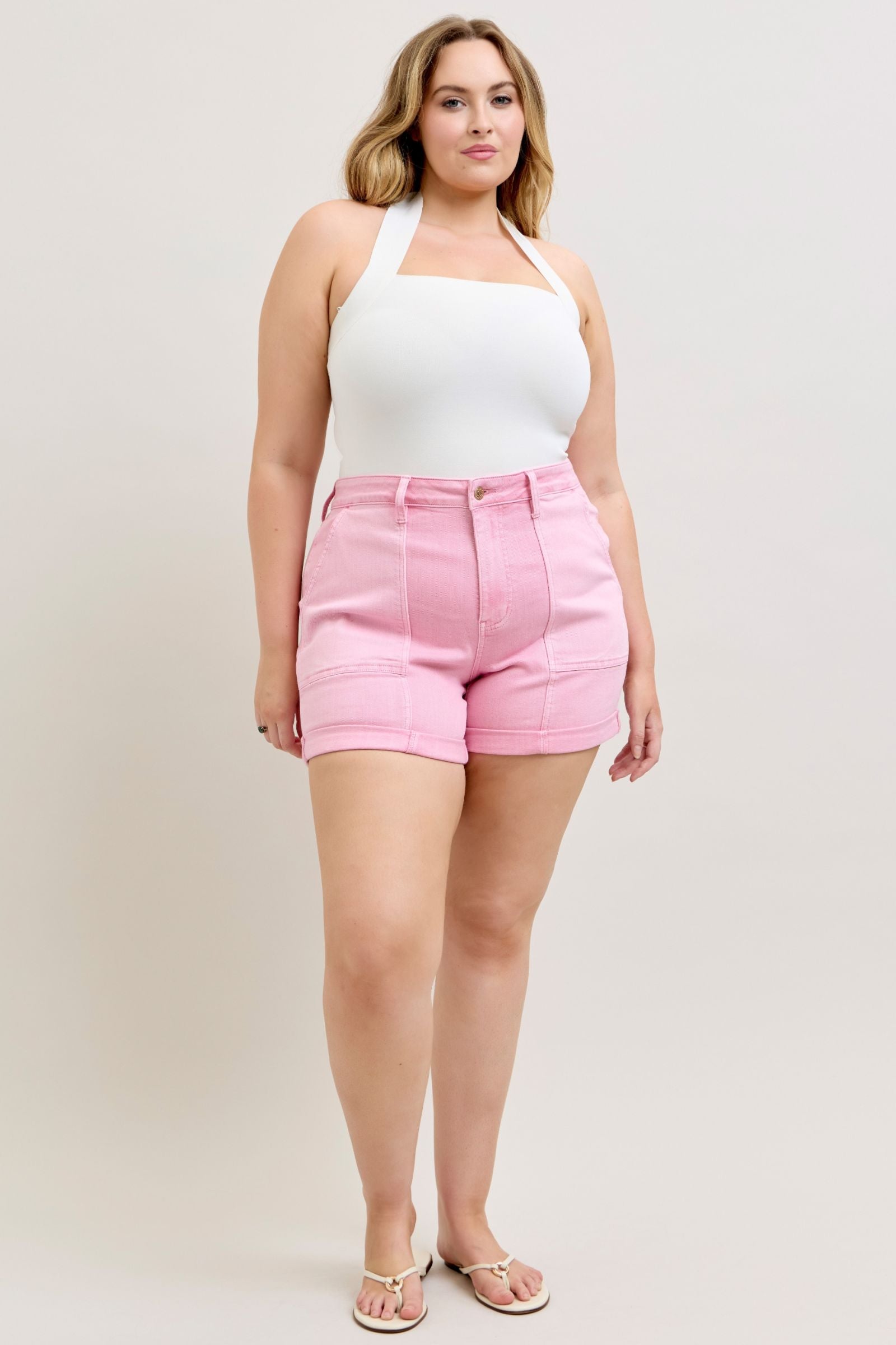 Woman wearing a white halter top and pink shorts on a plain background