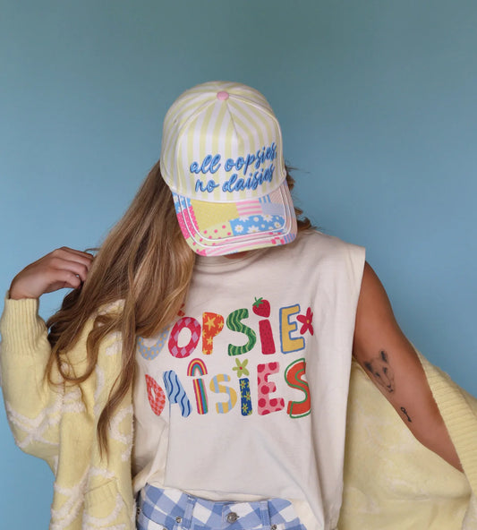 Person wearing a colorful 'Popsie Baisies' shirt, checkered shorts, and a matching cap against a blue background.