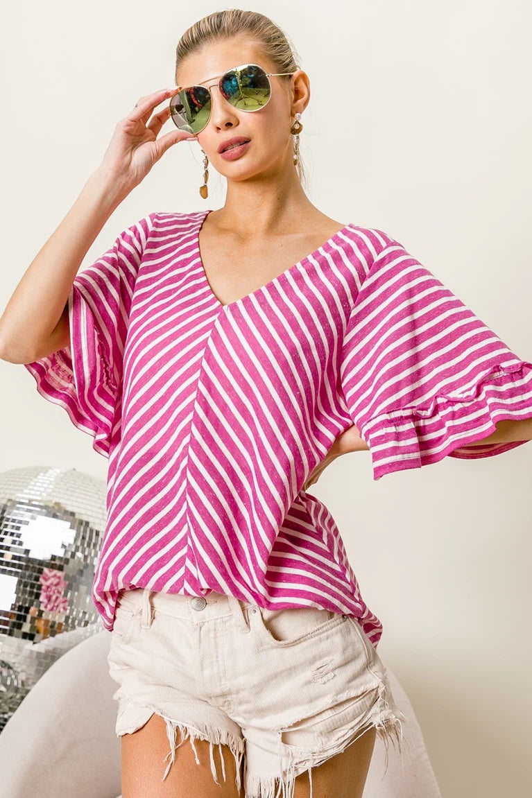 Woman wearing a pink and white striped top with white shorts, holding sunglasses.