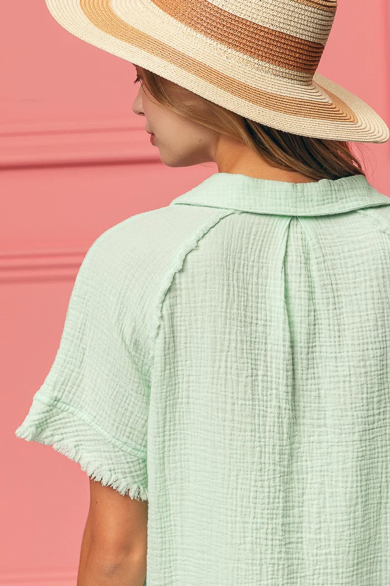 Person wearing a straw hat and light green textured shirt against a pink background