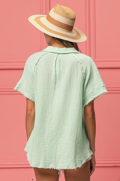 Person wearing a light green textured shirt and a straw hat against a pink wall.