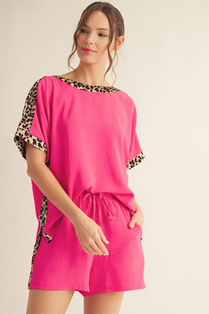 A model wearing a vibrant hot pink top with leopard print trim and matching shorts, both with a relaxed fit.